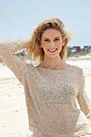 A young blonde woman on a beach wearing a beige kn