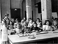 An Edwardian classroom scene, with young girls lea