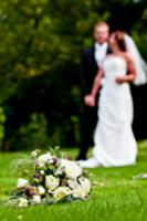 Bridal bouquet on lawn, bride and groom in backgro