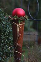 Rusty cone topped with large, red bauble framed wi