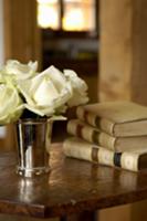 White roses in a silver cup and antique books on a