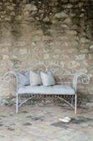 White garden bench with cushions against stone wal