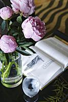 Glass vase with pink peonies next to open book and