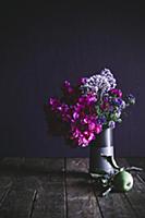 Vase of flowers and apple on wooden surface