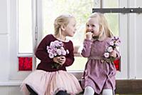 Two girls holding flowers sitting in front of peri