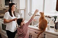Mother watching daughter play with cat on kitchen 