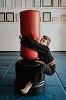 Boy clinging onto punch bag in martial arts studio