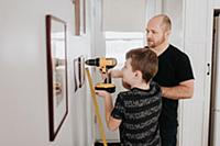 Father teaching son drill wall for picture frames