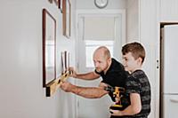 Father teaching son drill wall for picture frames