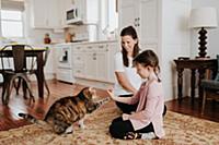 Mother watching daughter play with cat at home