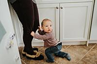 Baby boy in kitchen holding on to mother's legs