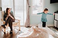 Mother watching toddler daughter jumping on cushio