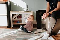 Baby boy sitting on living room rug next to father