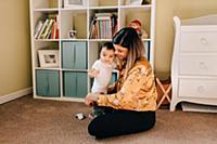 Mother sitting on nursery floor dressing baby son