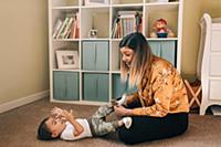 Mother sitting on nursery floor putting socks on b