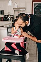 Girl in high chair feeding water melon to father