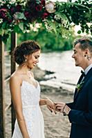 Groom putting on bride's ring on lakeside