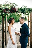 Groom putting on bride's ring on lakeside