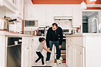 Girl playing with push toy in kitchen, father watc