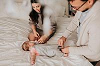 Couple dressing baby daughter on bed in bedroom