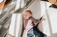 Baby boy lying on cushions on living room floor, o