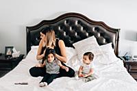 Baby boy sitting on bed while mother styles sister