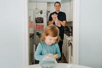 Female toddler at table and father in kitchen