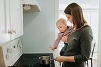 Mother carrying baby son while cooking at hob