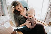 Baby boy sitting on mother's lap in living room, p