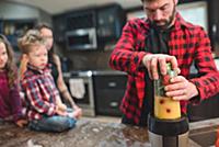 Mother and children watching father blend vegetabl