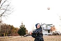 Boy hitting baseball ball in rural field, action