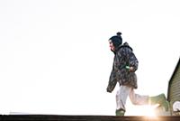 Boy in knit hat running across sunlit skateboard r