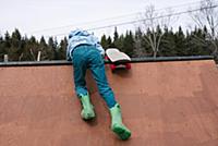 Boy clambering to top of skateboard ramp, rear vie