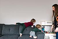 Mother watching over sons playing on sofa