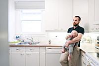 Father bottle feeding baby son in kitchen