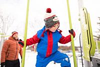 Boy with father climbing up playground slide in sn