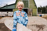 Blond boy carrying skateboard in farmyard, portrai
