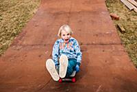 Boy sitting and skateboarding backwards down woode