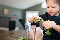 Toddler peeling vegetable into blender