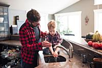 Father watching son wash hands in kitchen sink