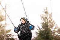 Boy in knit hat swinging on playground swing in wi