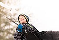 Boy in knit hat swinging on playground swing in wi