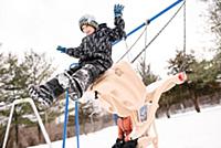 Boy jumping from playground swing in snow