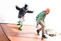 Boy chasing father on skateboard ramp, low angle v