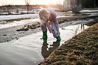 Boy rolling trousers up in rural meltwater puddle
