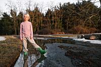 Boy standing ankle deep in rural meltwater puddle,