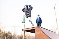 Girl watching brother jump from top of skateboard 