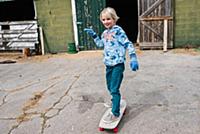 Blond boy skateboarding in farmyard