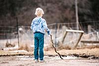 Blond boy on wasteland playing with tree branch in