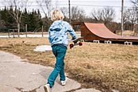 Blond boy carrying skateboard toward rural skatebo